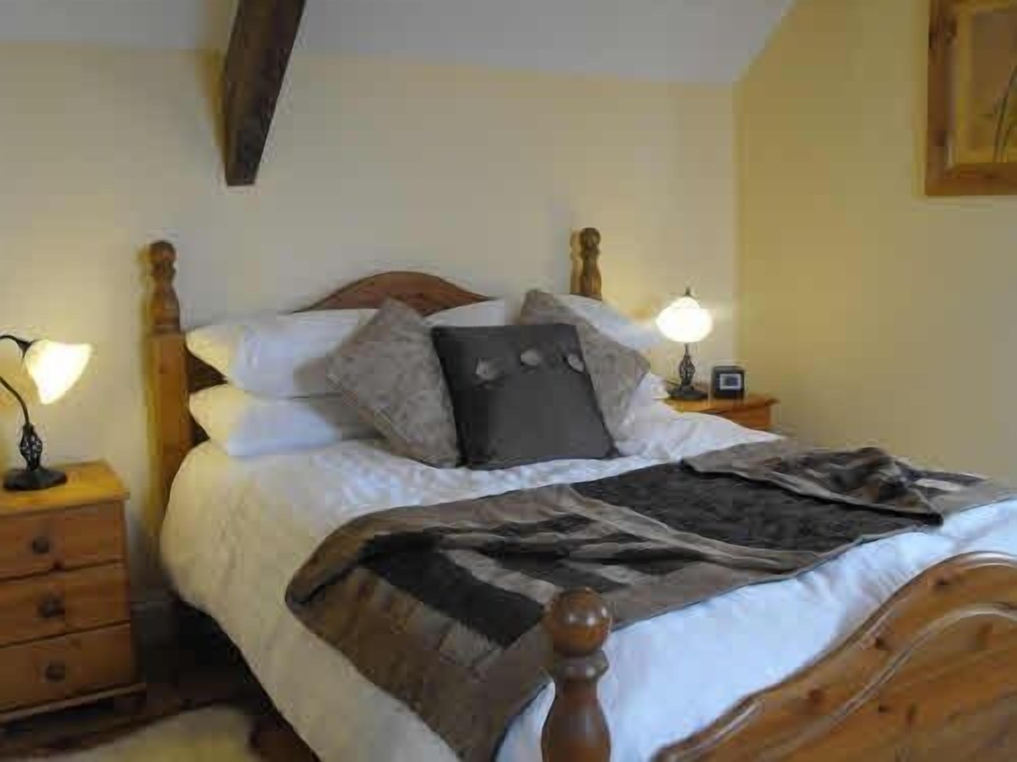 A bedroom with a wooden bed frame, white bedding, and two bedside lamps.