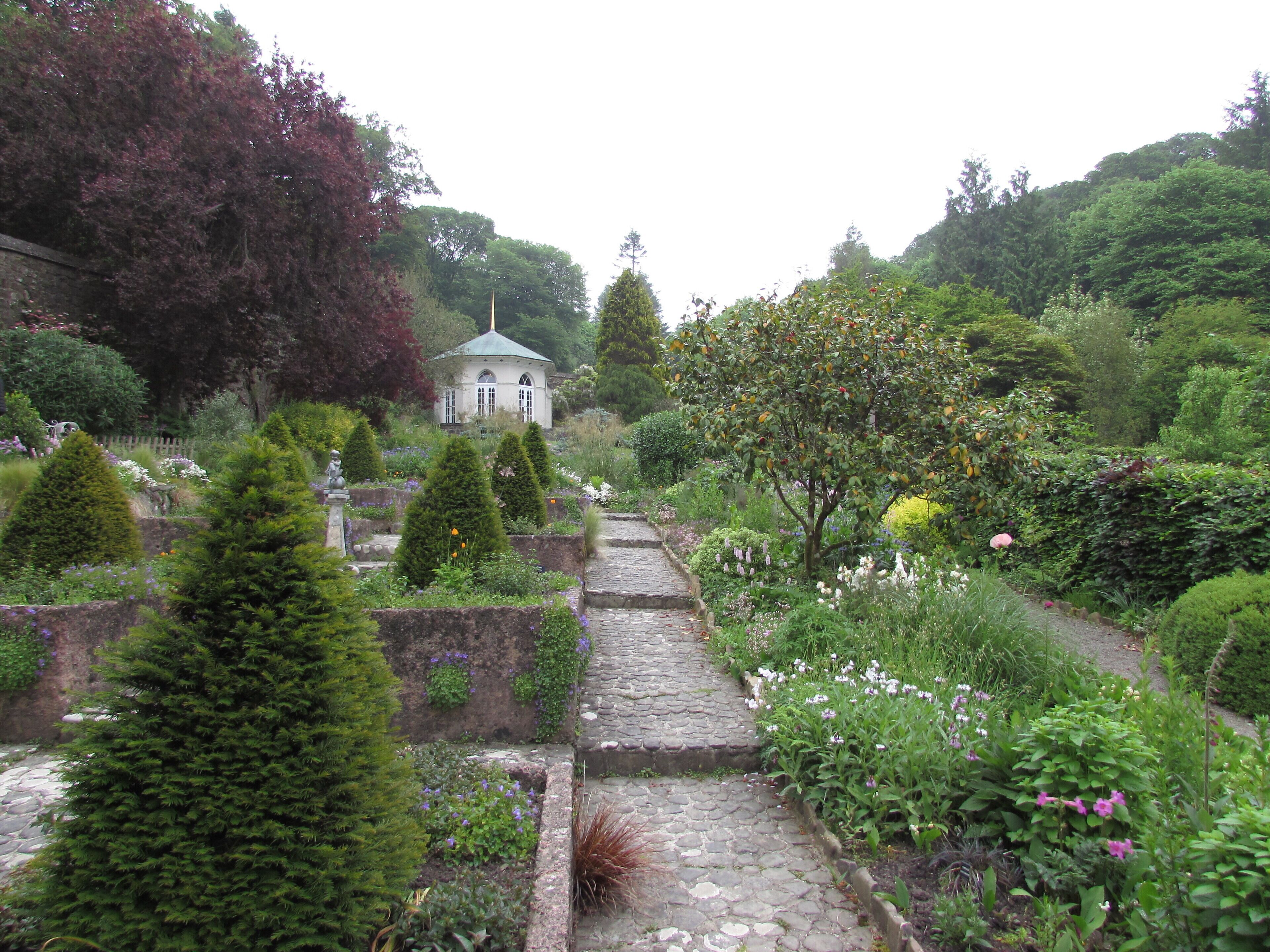 A garden pathway leading to a white gazebo surrounded by various plants and trees.