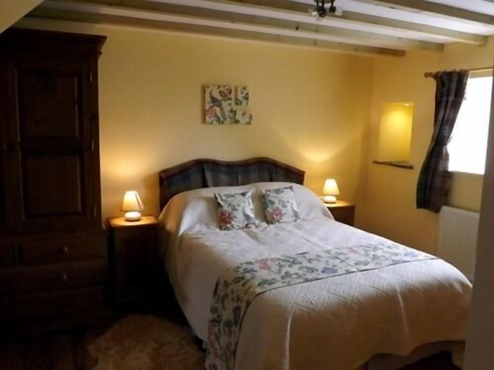 Una camera da letto con una testiera in legno, una coperta con motivi floreali, due abat-jour e un quadro appeso al muro.