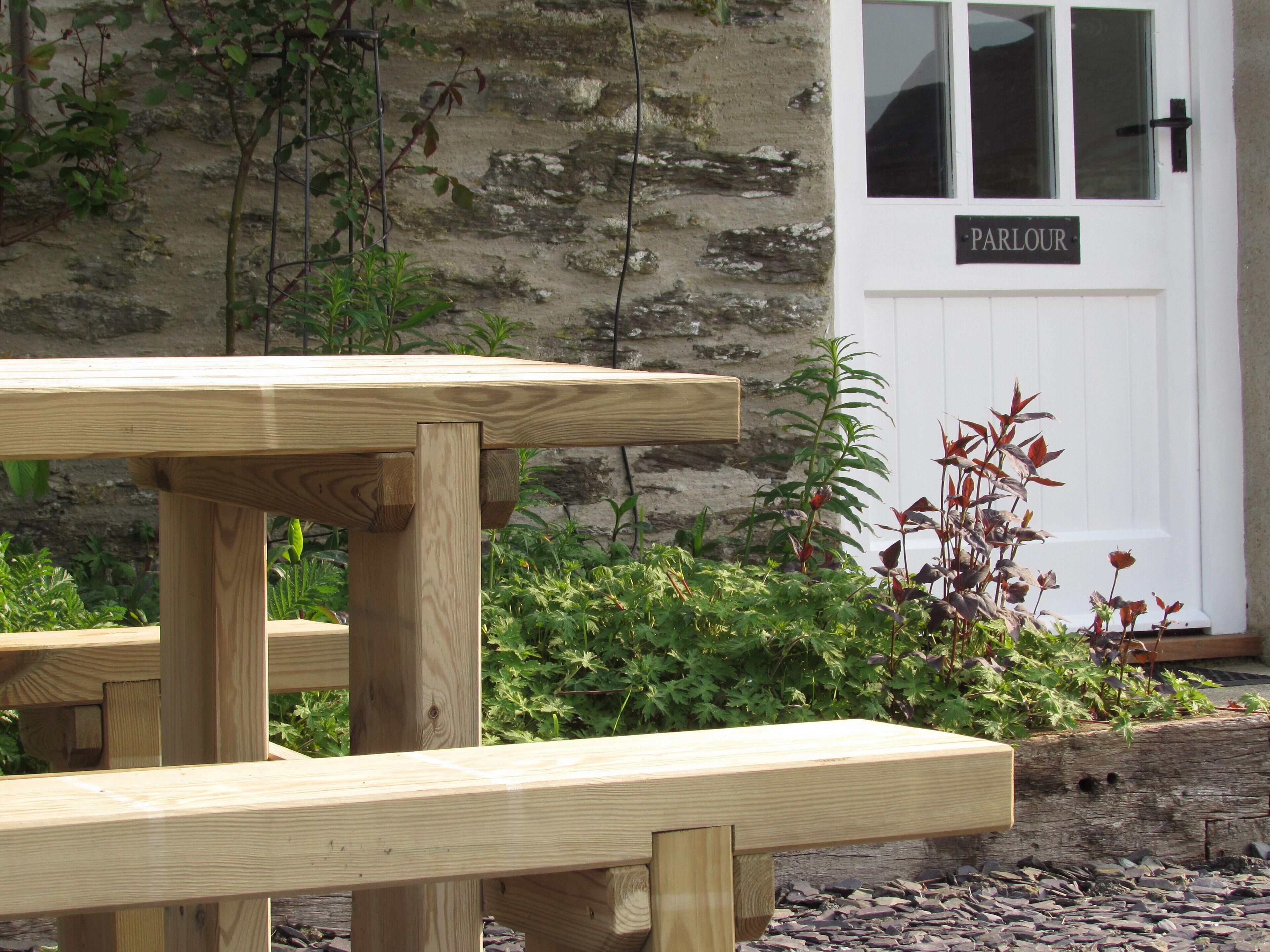 A wooden picnic table in front of a stone building with a door labeled "PARLOUR".