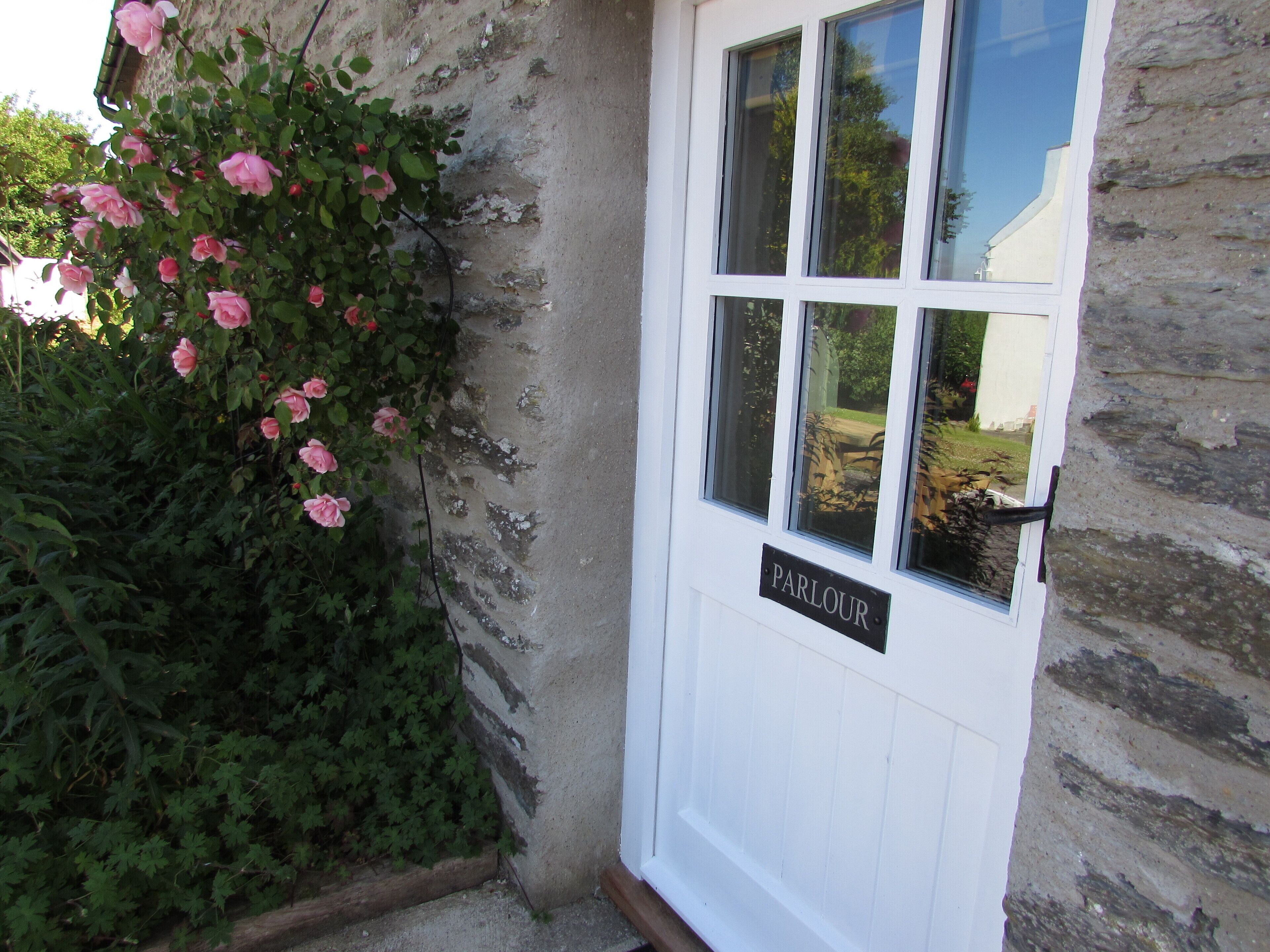 A white door with a sign reading "PARLOUR" and a window reflecting a garden scene.