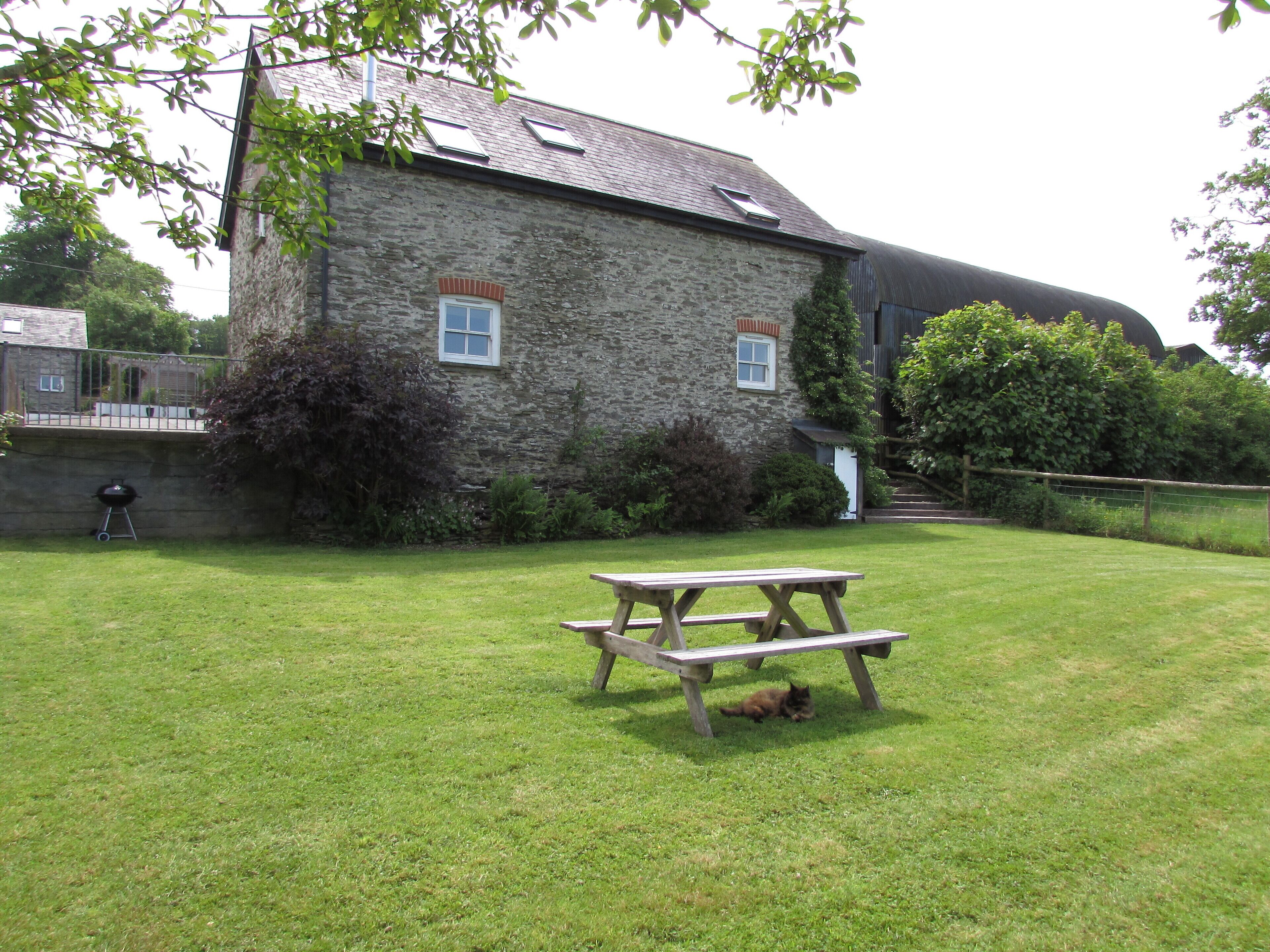 Un bâtiment en pierre avec une table de pique-nique dans une cour verdoyante.