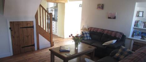 A cozy living room with a wooden staircase, a sofa, a coffee table, and a bookshelf.