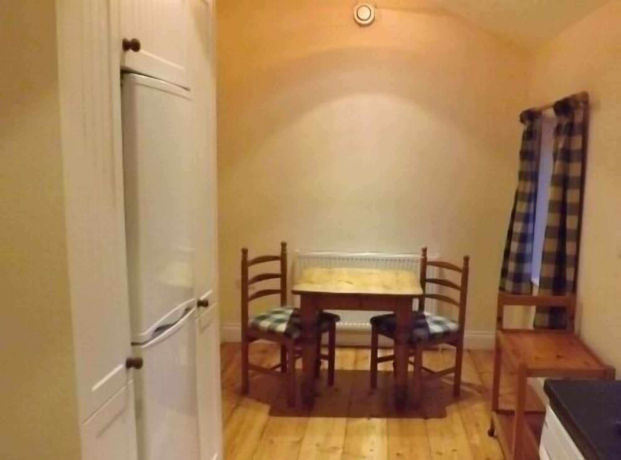 A small kitchen with a table and chairs, a refrigerator, and a window with curtains.