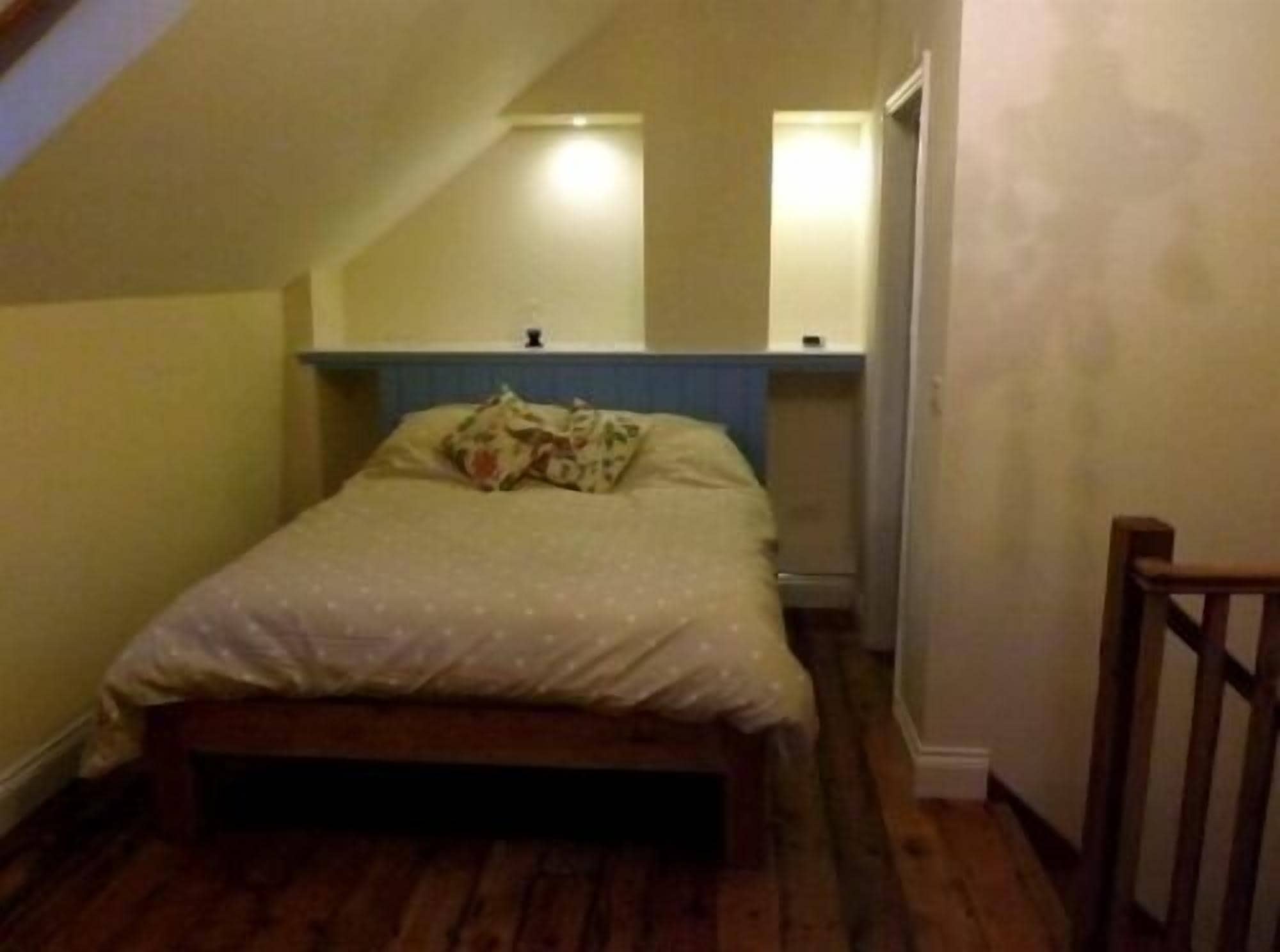 A small, cozy bedroom with a single bed, a wooden headboard, and a sloped ceiling.