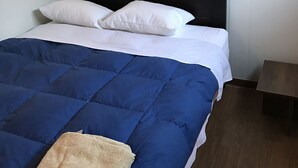 A neatly made bed with a blue and white duvet, a wooden headboard, and a small bedside table. - Bamboo Paracas Resort (Paracas)