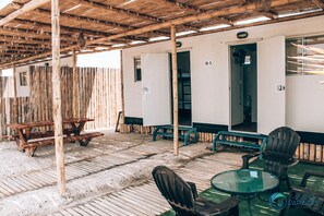 A covered outdoor area with wooden tables and chairs, a glass table, and a bamboo fence. - Bamboo Paracas Resort (Paracas)
