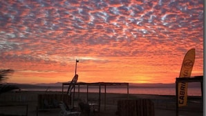 A beach scene with a wooden structure, a flag, and a surfboard. - Bamboo Paracas Resort (Paracas)