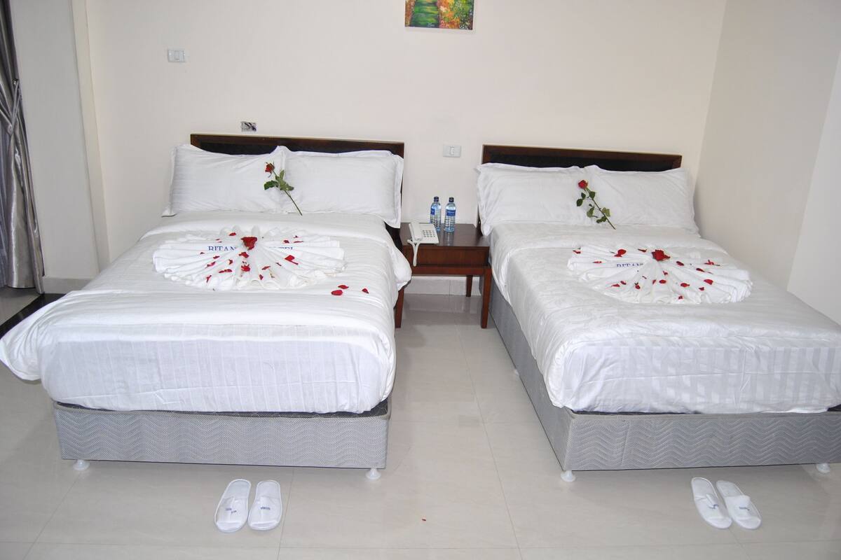 Two single beds with white bedding, a small bedside table with a phone, and a pair of slippers on the floor.