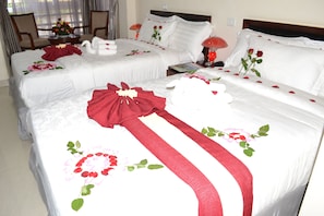 Two plush beds, each with white linens and red floral decorations, are positioned side by side.