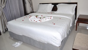 A neatly made bed with white linens and rose petals arranged on the bedspread.