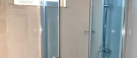 A corner bathroom with a glass-enclosed shower, a toilet, and a sink.