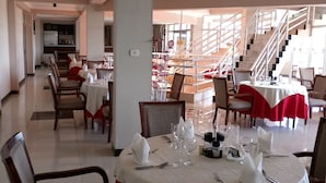 A dining area with tables set for four, chairs, and a staircase in the background.