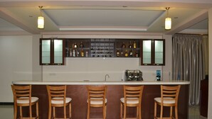A bar area with a long counter, four wooden bar stools, and a variety of bottles and glasses on shelves above.