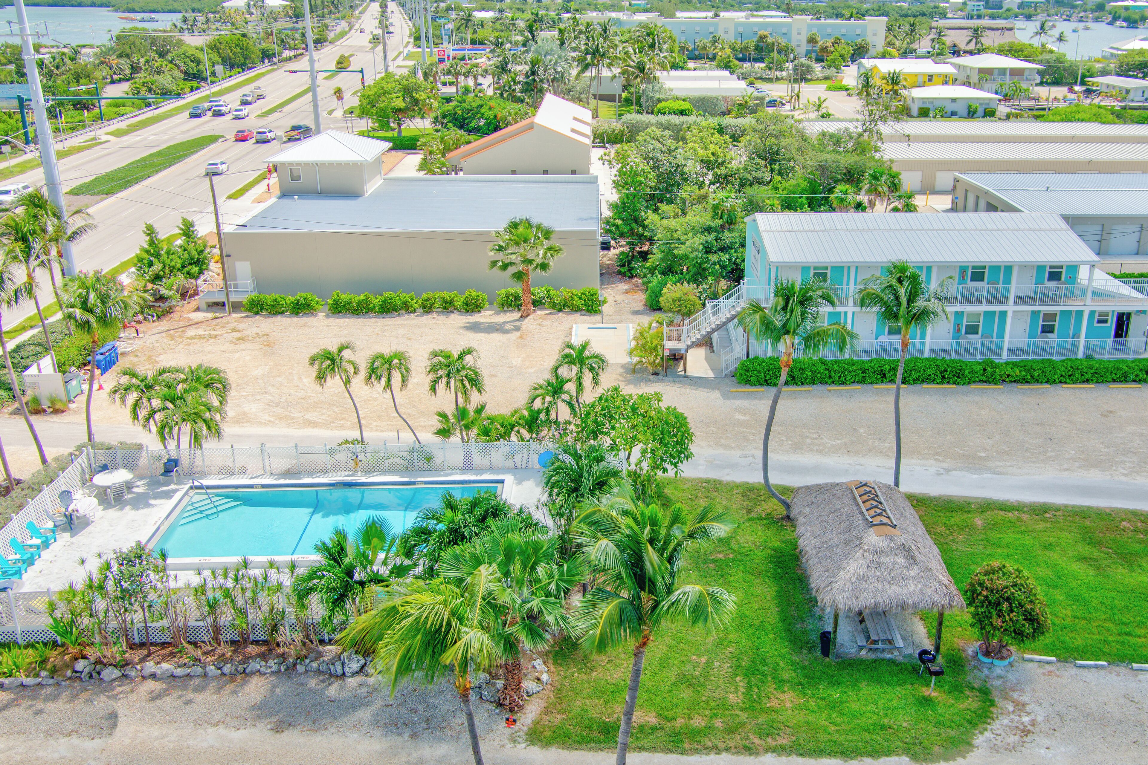 Luchtbeeld van een resort met een zwembad, palmbomen en strandwoningen.
