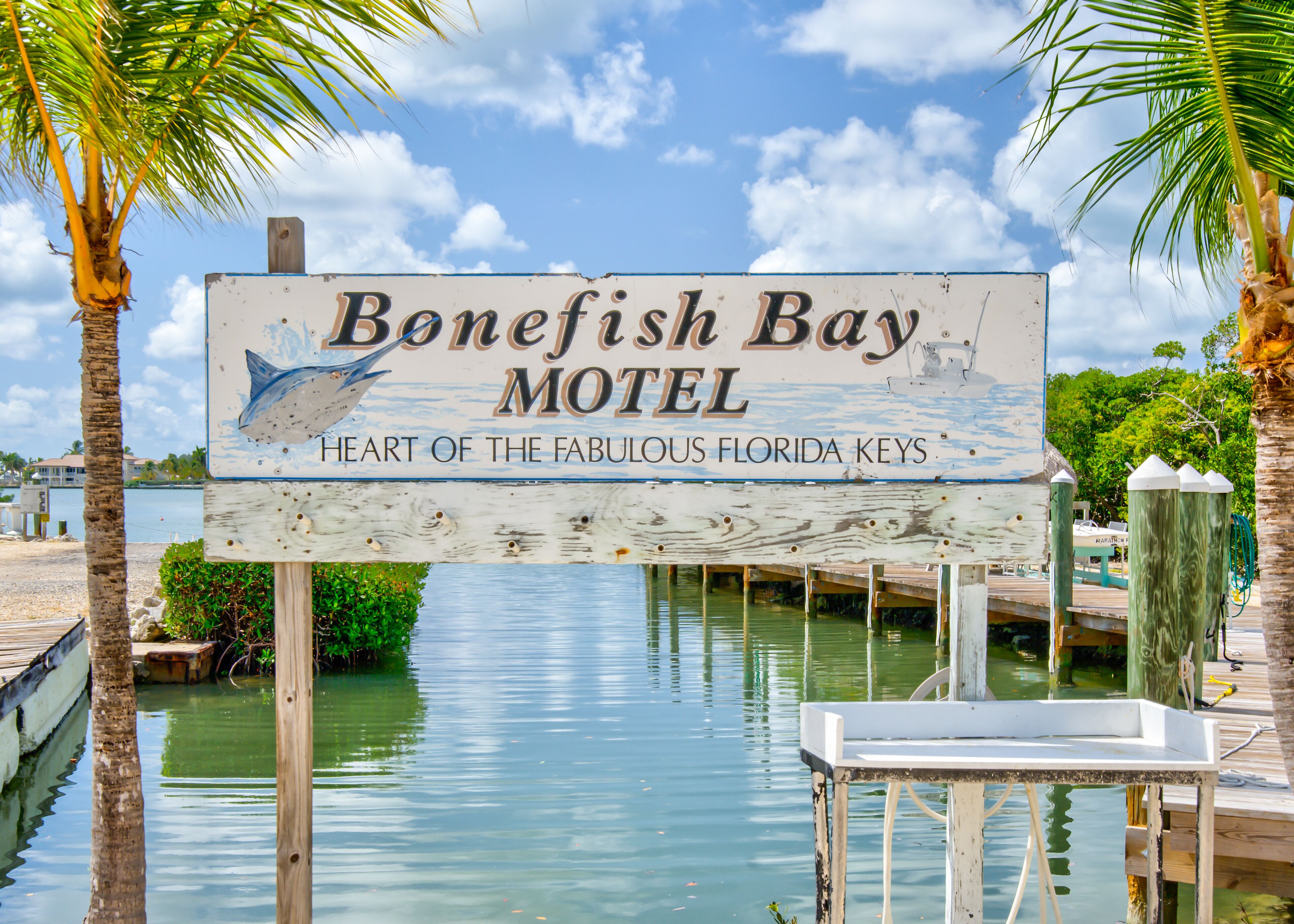 Une enseigne pour le motel Bonefish Bay, ornée d’une illustration de dauphin, située au bord de l’eau, avec des palmiers et un quai.