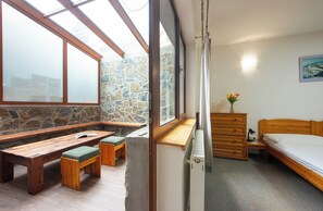 Ein Schlafzimmer mit Steinswand, Holzmöbeln, einem Bett, einem Nachttisch und einem Fenster mit Blick zum Himmel.