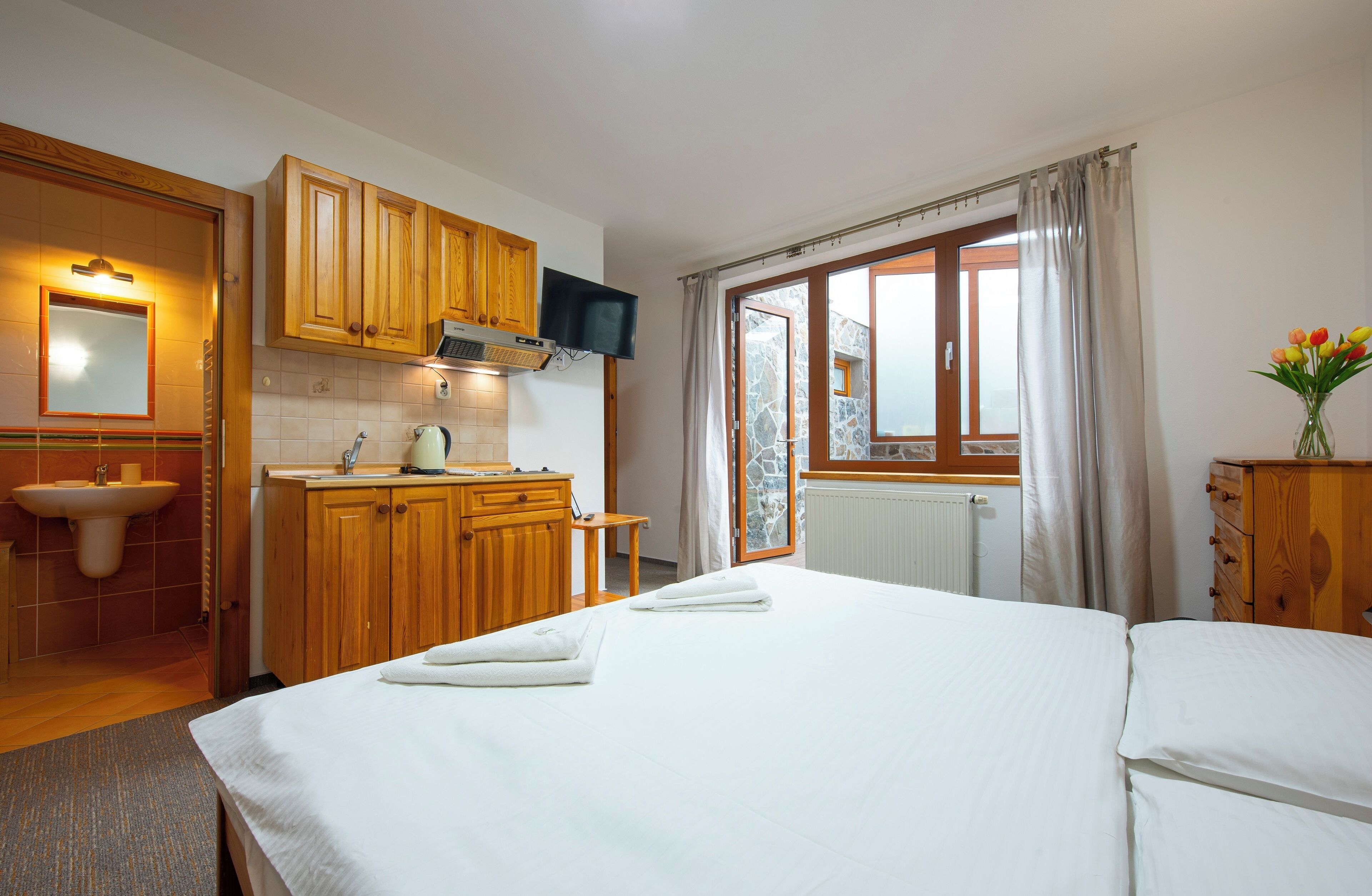 Quarto de hotel com cama, banheiro com pia e área de cozinha.