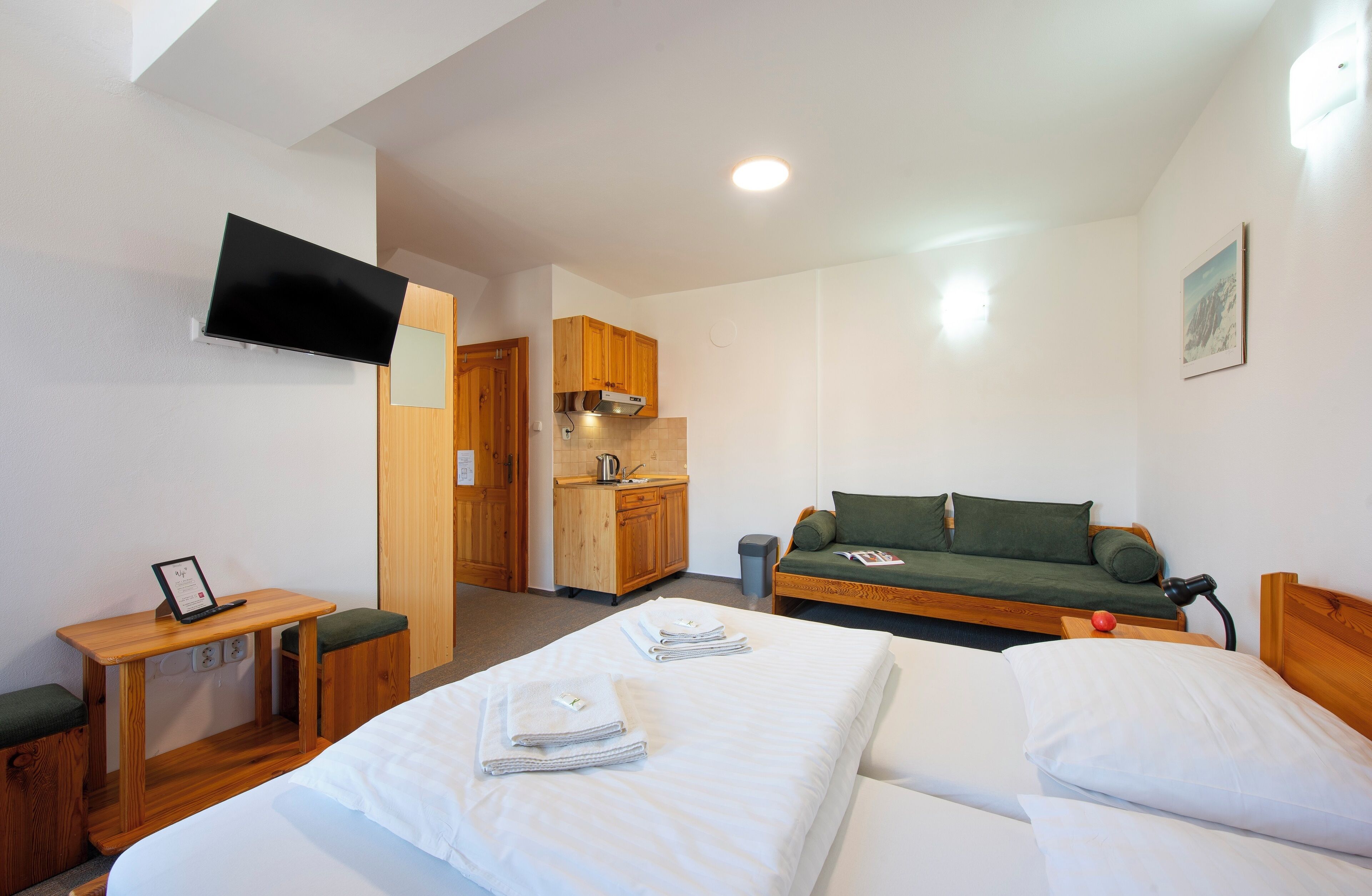 Habitación de hotel con cama, escritorio, televisor, kitchenette y sofá.
