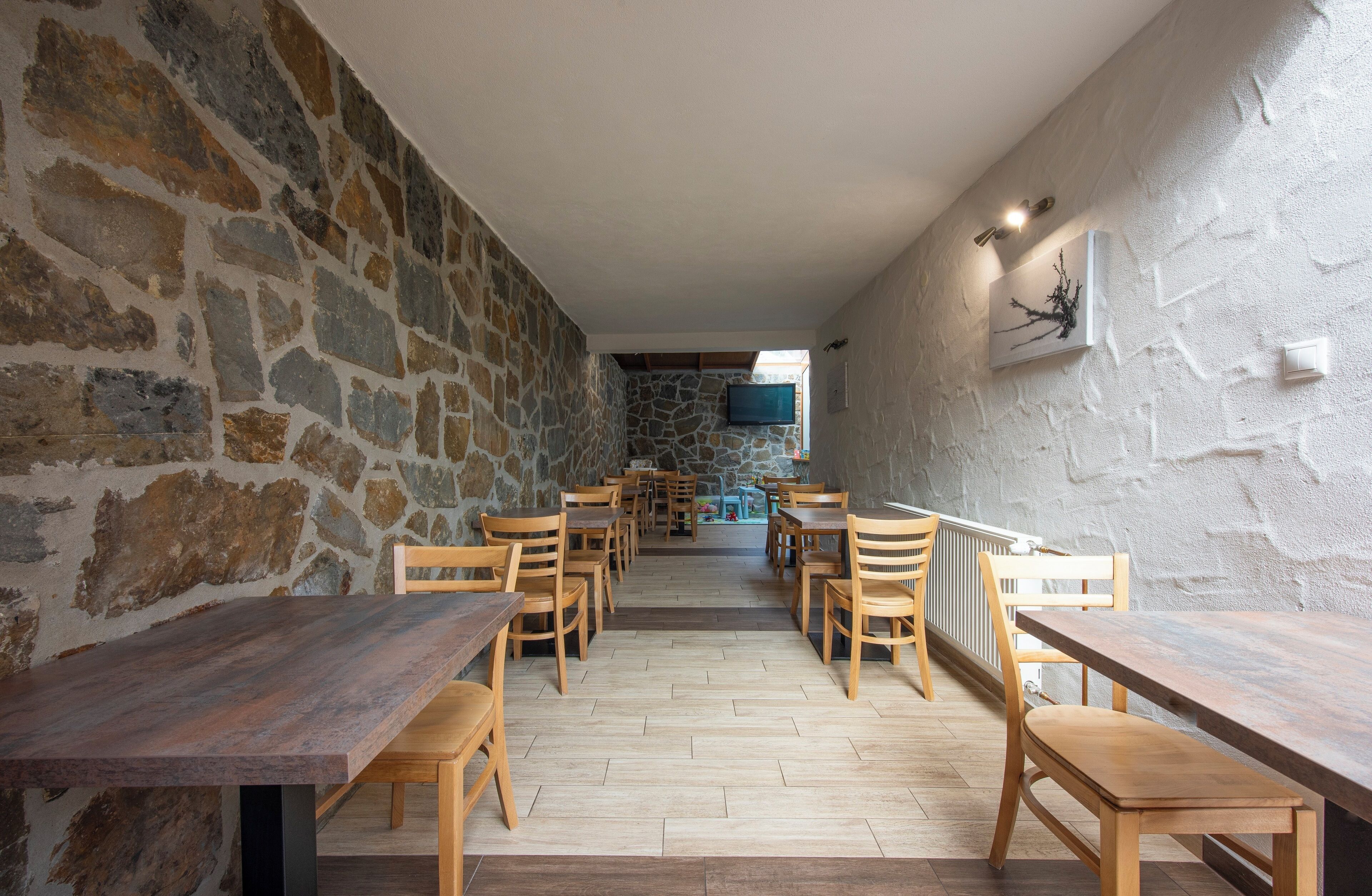 Un restaurante con paredes de piedra, mesas y sillas de madera, y un televisor en la pared.