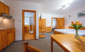 Ein kleines Hotelzimmer mit Holzmöbeln, einer Küchenzeile, einer Dusche und einem Bett mit einer Vase voller Tulpen.