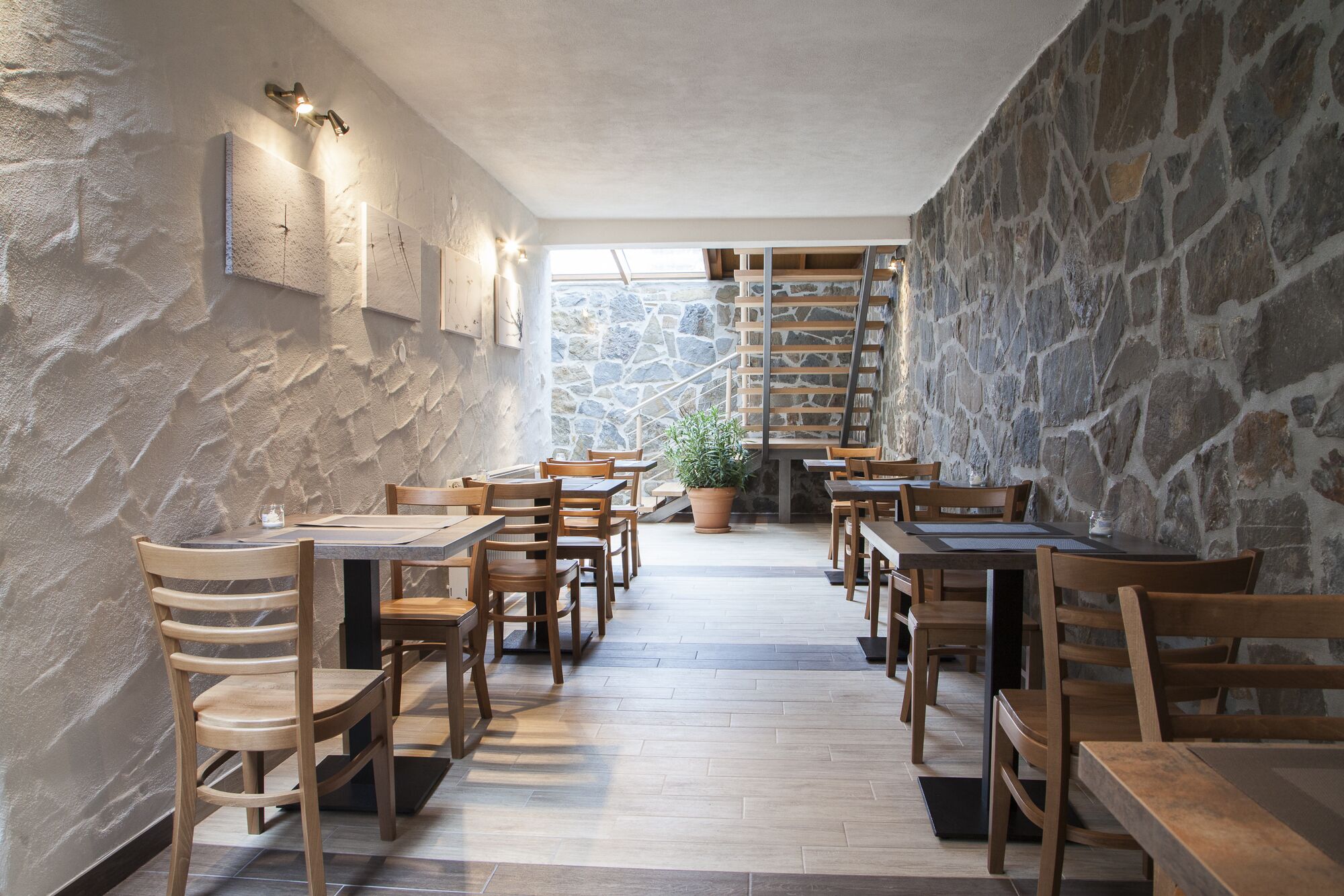 Een restaurant met houten tafels en stoelen, stenen muren en een trap naar een hoger niveau.