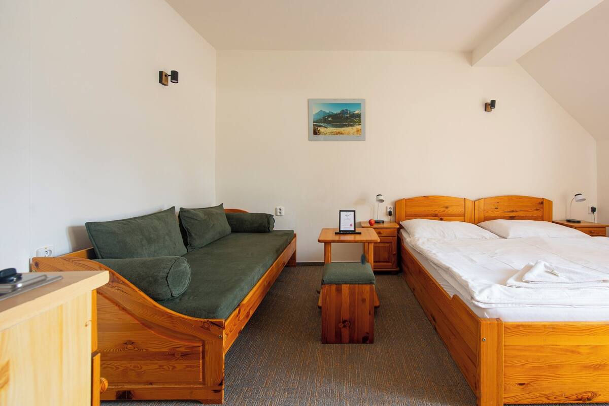 Una habitación con una cama y un sofá de madera, una mesita pequeña y un cuadro colgado en la pared.