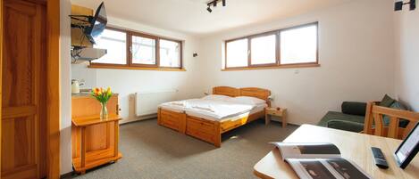 A bedroom with a wooden bed, a desk with a lamp, a chair, and a window.