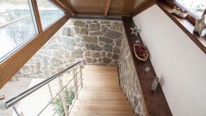 A wooden staircase with stone walls, a metal railing, and a shelf with decorative items.