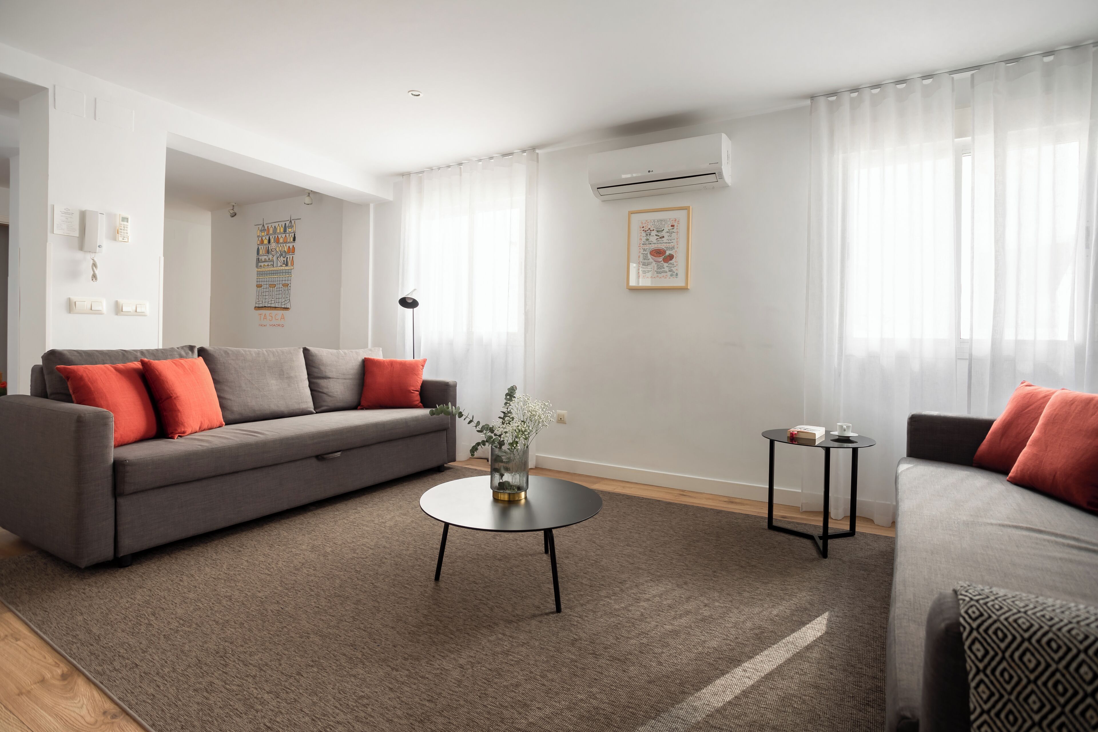 Een moderne woonkamer met een grijze bank, een ronde salontafel en een bijzettafeltje.