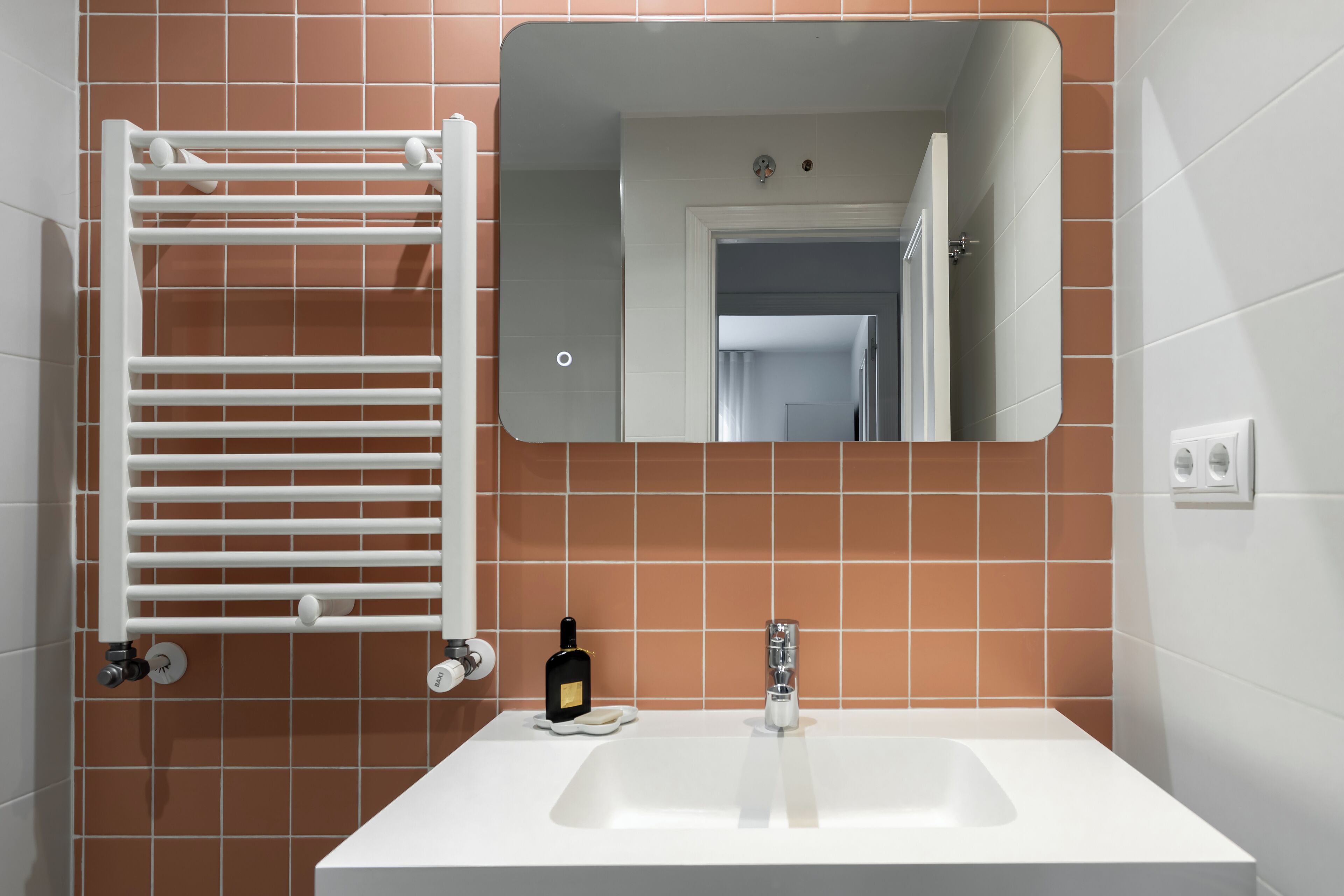 Un baño con un lavamanos blanco, un espejo y un perchero para toallas.