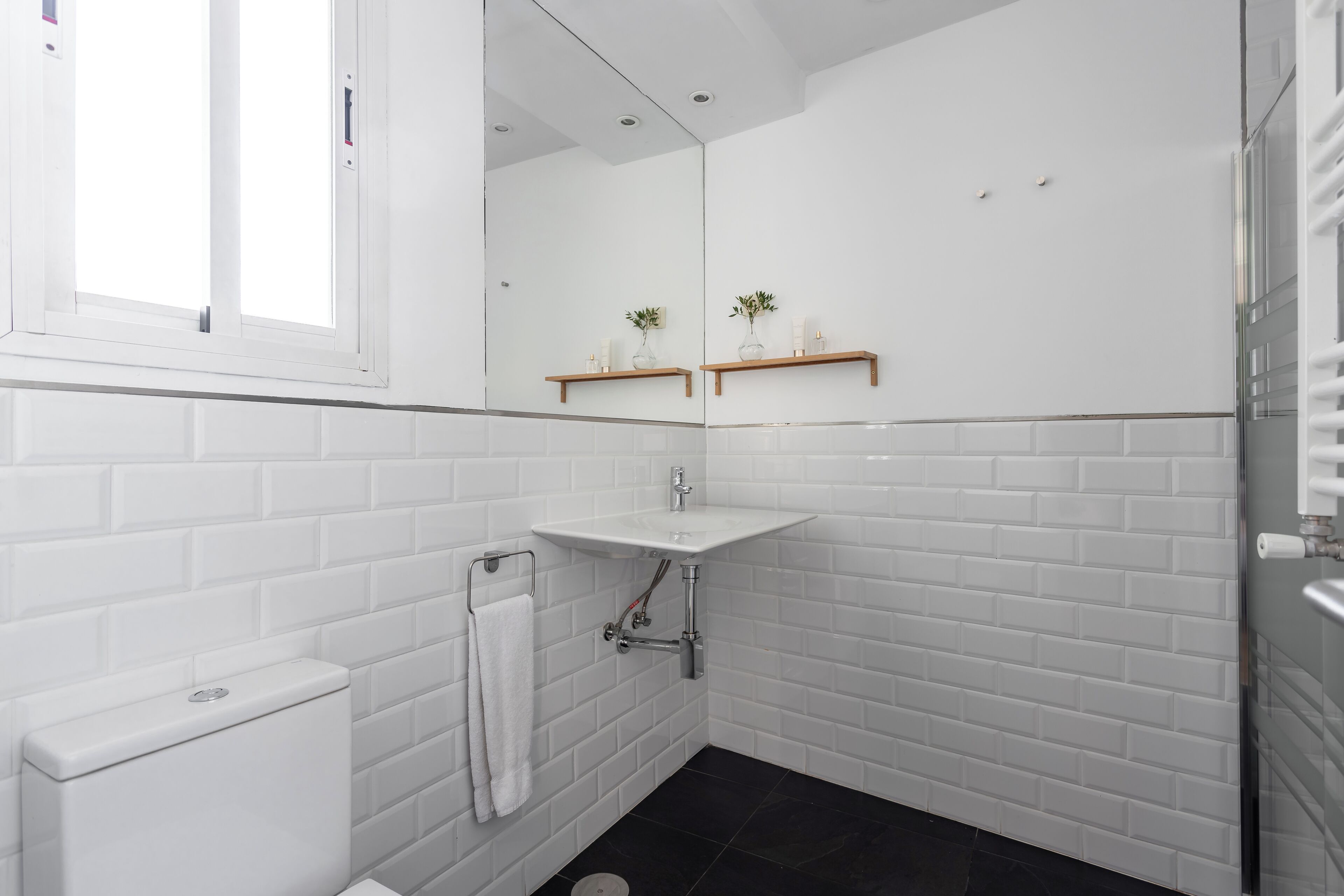 Een badkamer met witte metrotegels, een witte wastafel, een spiegel en een raam.