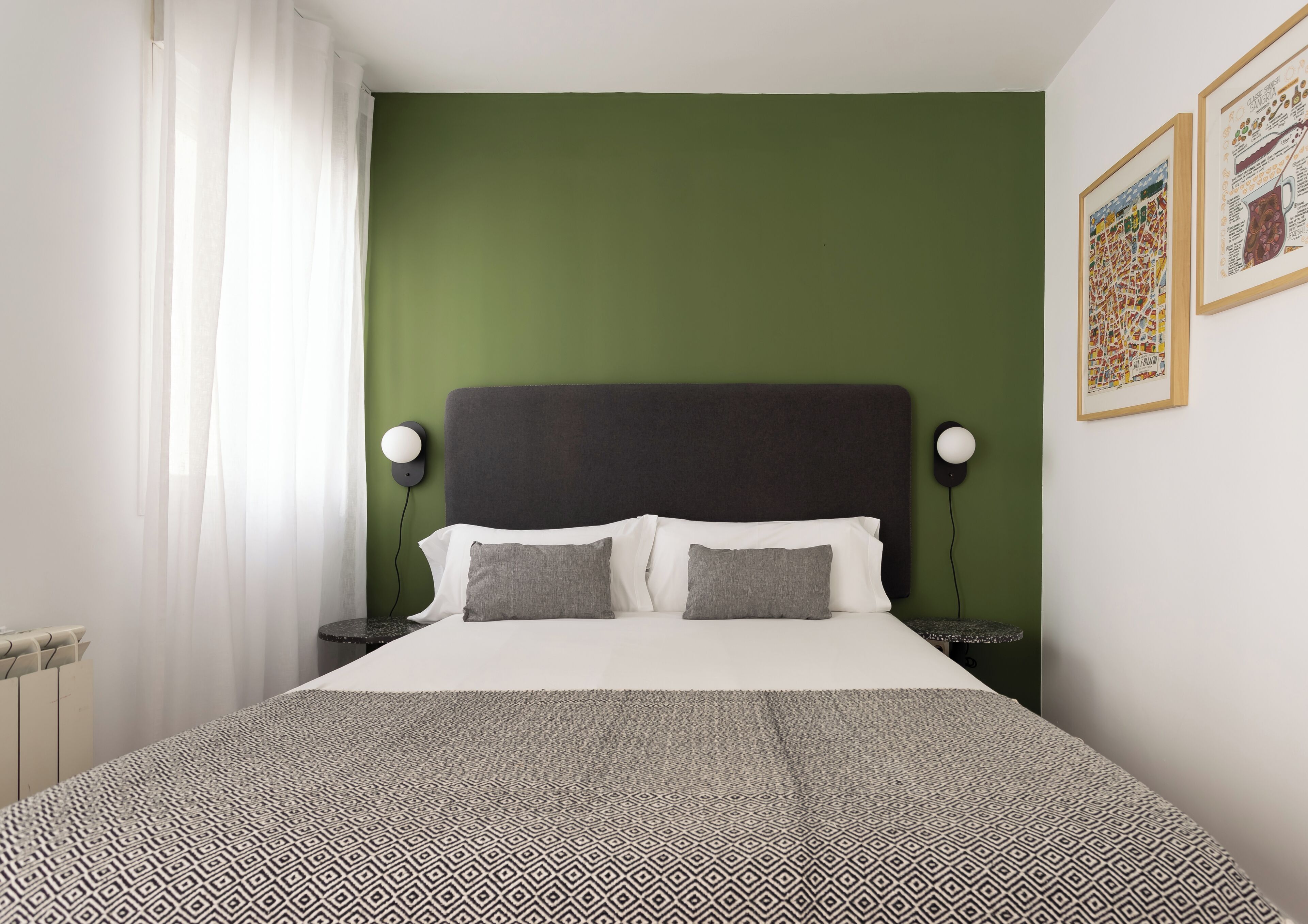 Ein Schlafzimmer mit einem Bett, zwei Nachttischen, einer grünen Wand und zwei gerahmten Bildern.