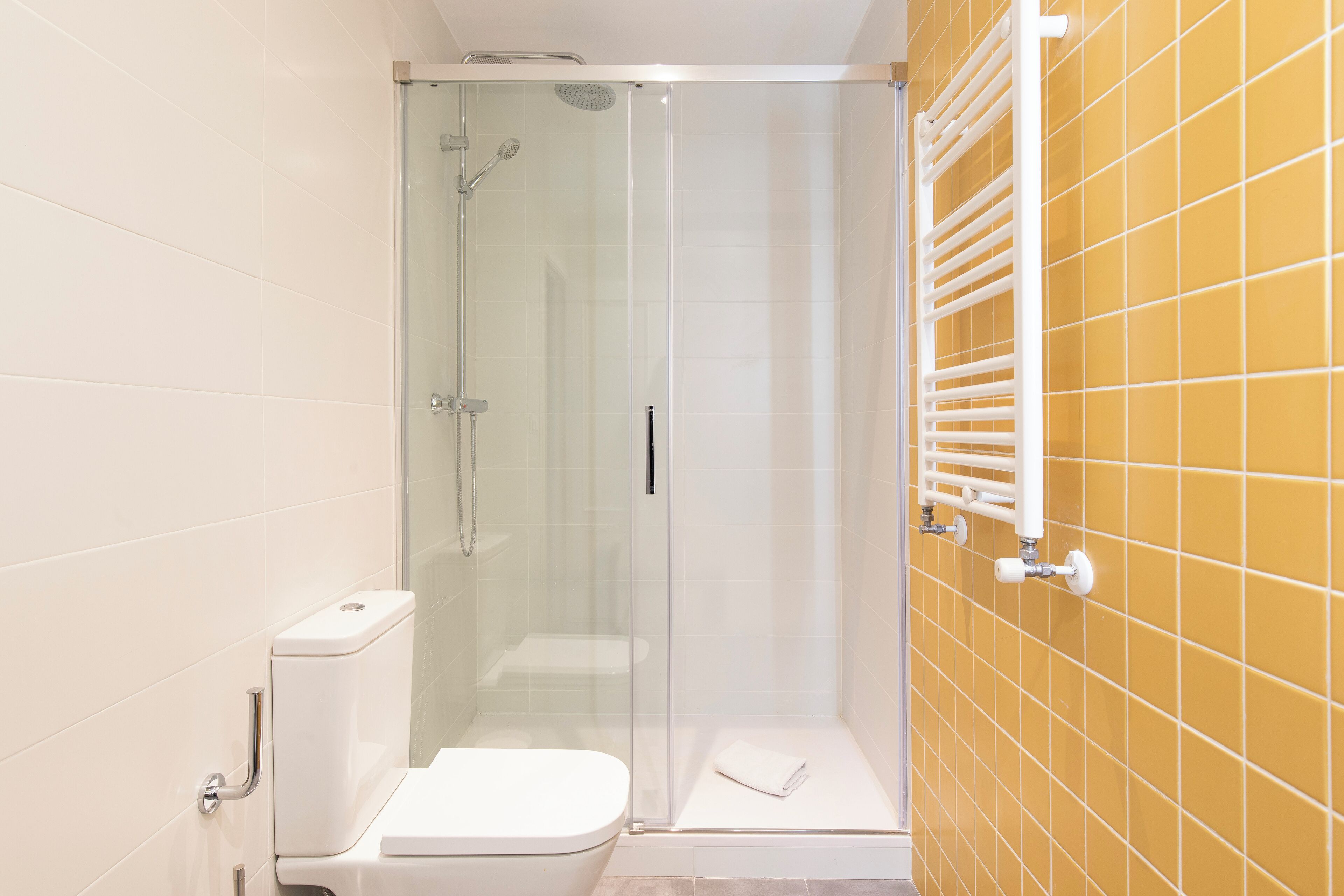 A bathroom with a glass-enclosed shower, a white toilet, and a yellow-tiled wall.