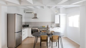 Una cocina moderna con un refrigerador de acero inoxidable, microondas y horno, sillas de madera y una mesa de comedor.