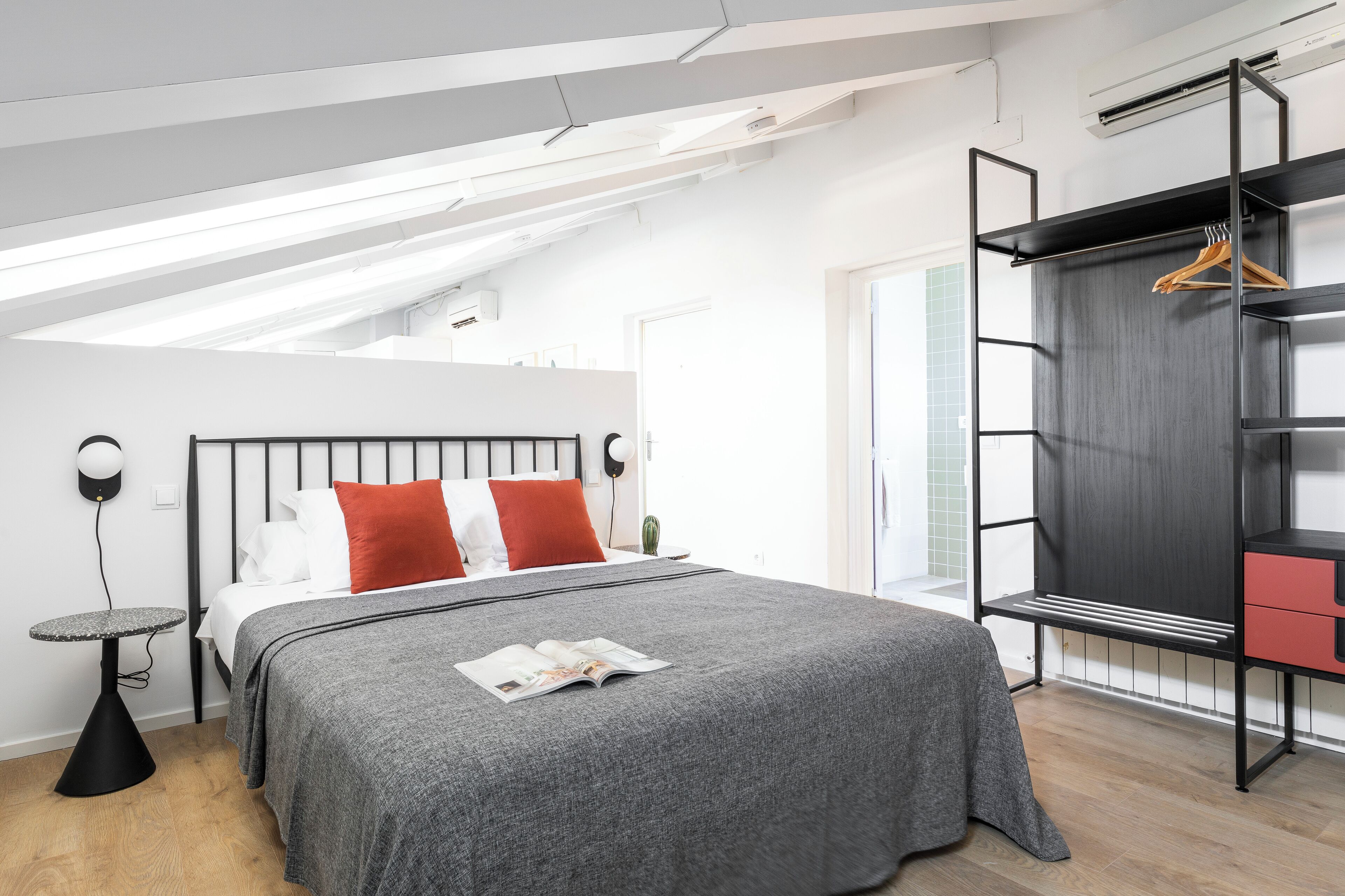 Une chambre à coucher moderne, avec un lit, une table de chevet, une armoire suspendue et un puits de lumière.