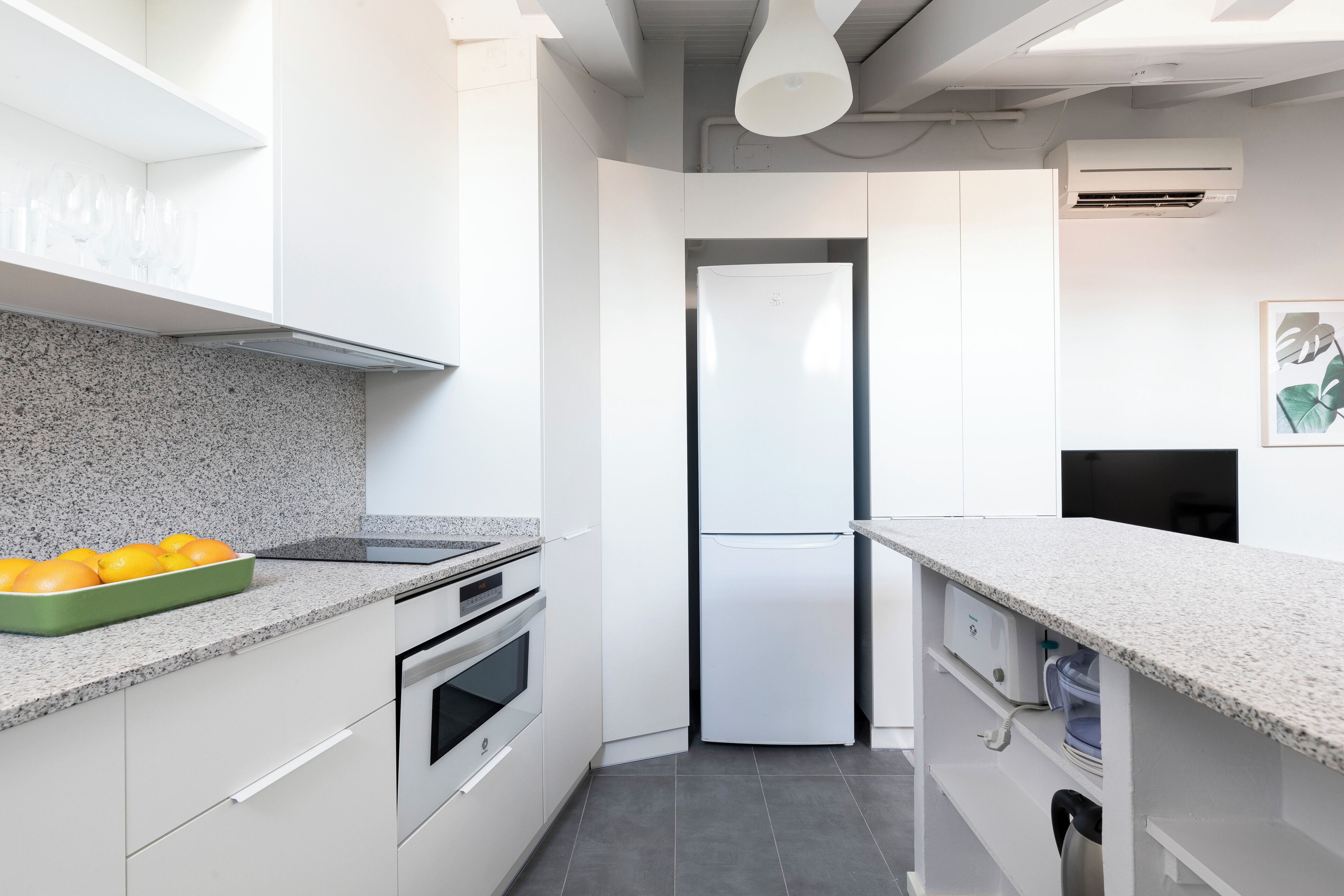 Una cocina moderna con armarios blancos, encimera de granito, horno integrado y refrigerador de acero inoxidable.
