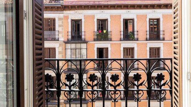 Un balcón con barandilla de hierro forjado y detalles florales, que da a una hilera de edificios con balcones y ventanas.