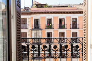 Ein Balkon mit schmiedeeisernen Geländern und floralen Verzierungen, mit Blick auf eine Reihe von Gebäuden mit Balkonen und Fenstern.