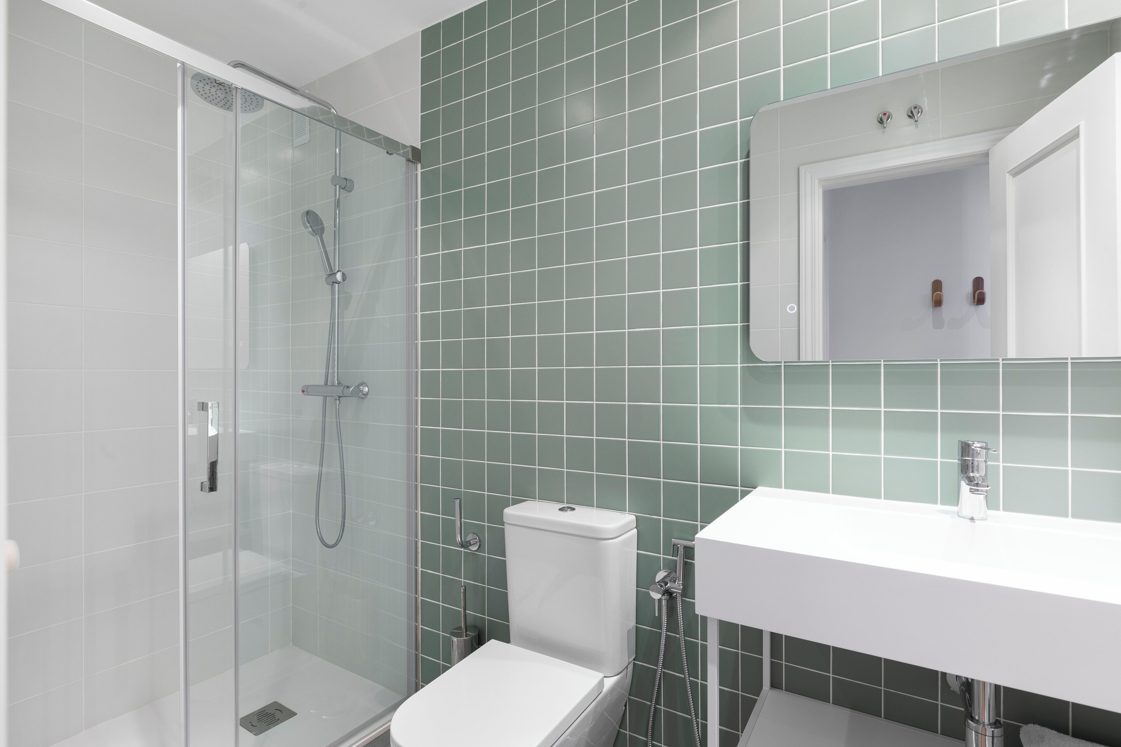 Un baño moderno con ducha envuelta en vidrio, inodoro blanco y lavabo blanco con espejo superior.