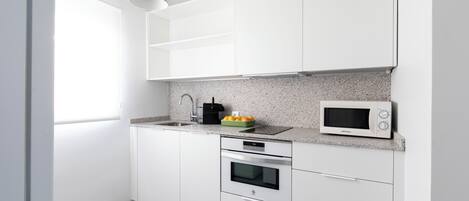 A modern kitchen with white cabinets, a granite countertop, a microwave, an oven, and a green pendant light.