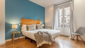Un dormitorio con cabecera de madera, una cama con almohadas y una colcha, una mesita de noche con una lámpara y una silla.