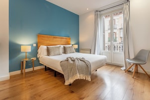 Ein Schlafzimmer mit einem hölzernen Kopfende, einem Bett mit Kissen und Decke, einem Nachttisch mit Lampe sowie einem Sessel.