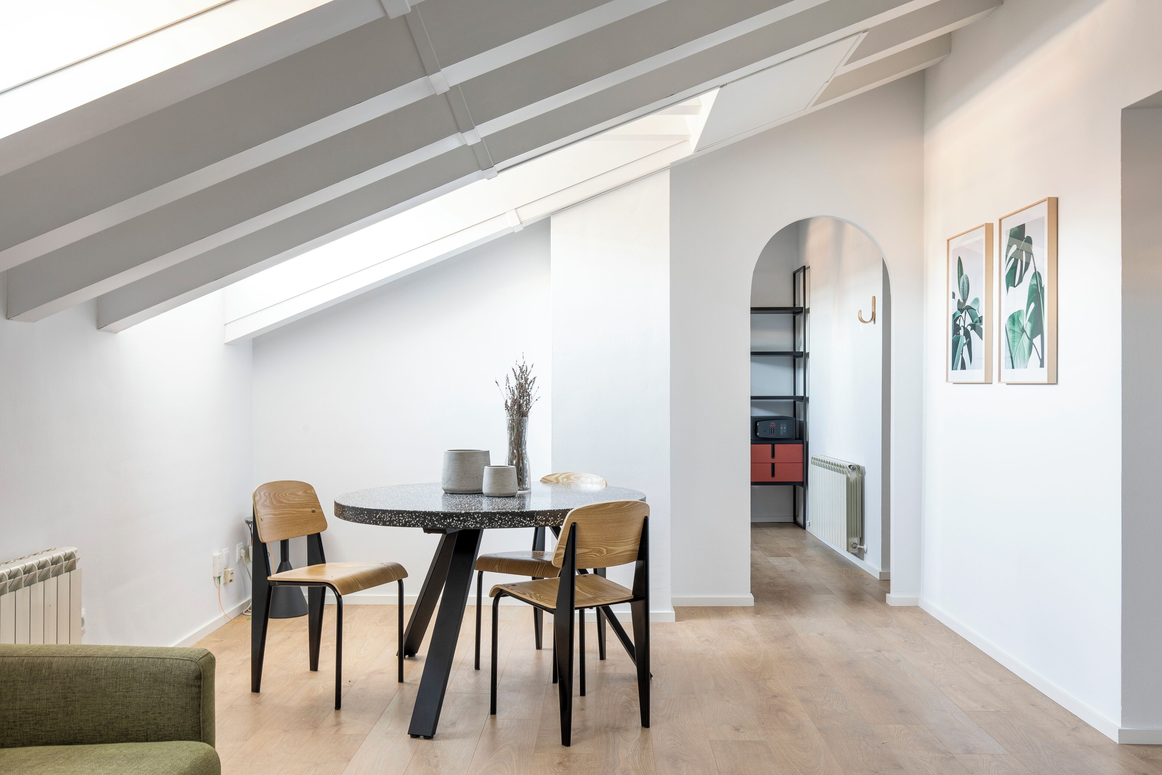 A modern dining area with a round table, two chairs, and a skylight above.