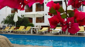 A poolside area with lounge chairs and umbrellas, a clear blue pool, and a building with balconies in the background. - TURISMO BRACAMONTE SAC (Huanchaco)