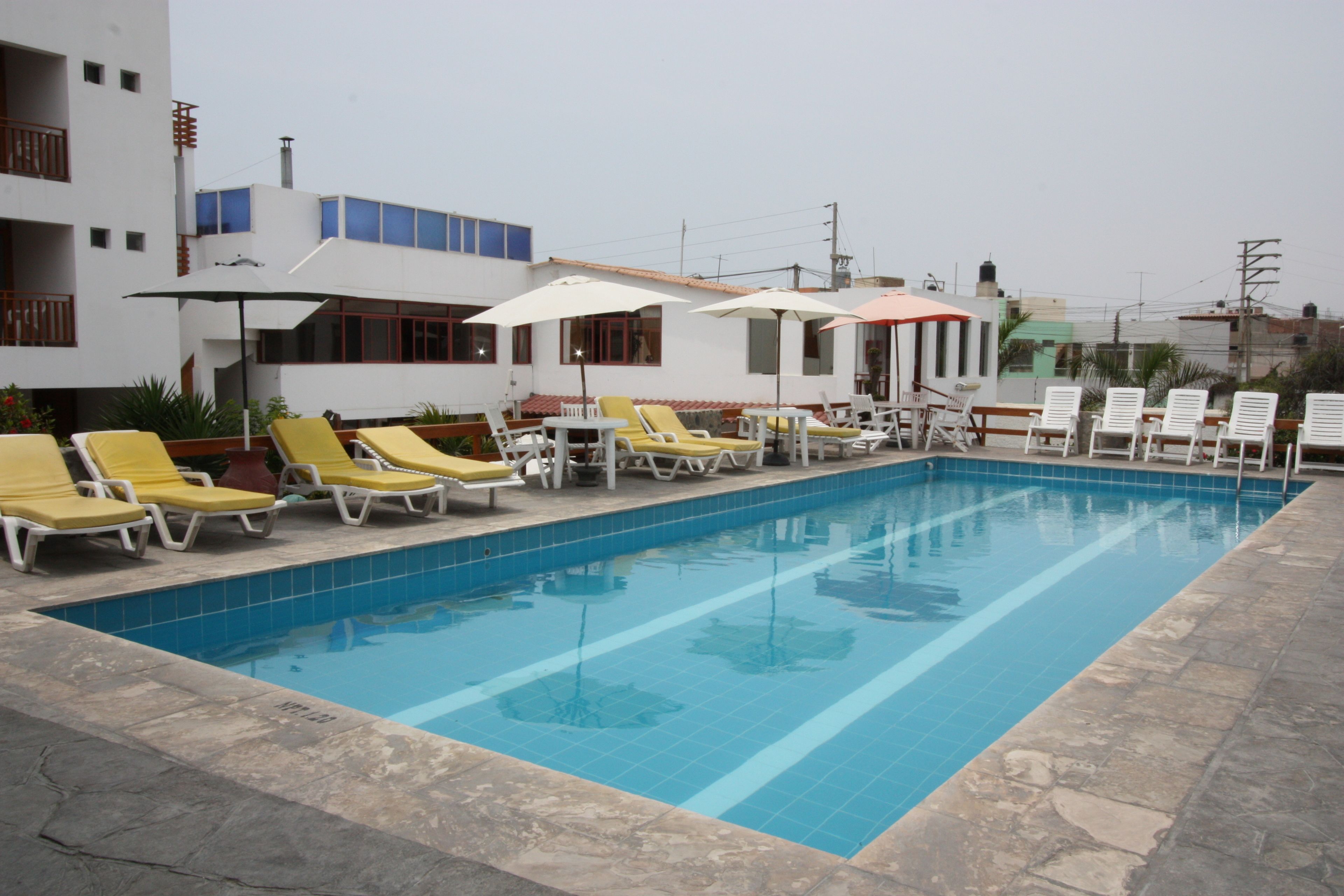 A swimming pool with sun loungers and umbrellas, surrounded by a building with balconies and windows.