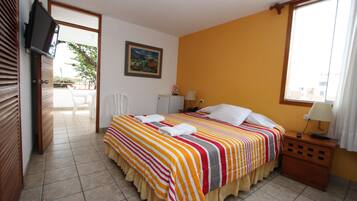 Habitación de hotel con cama, televisión, ventana y puerta que da a un balcón.
