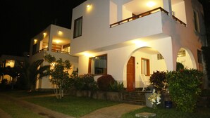 A modern two-story house with a well-lit entrance and a small porch. - TURISMO BRACAMONTE SAC (Huanchaco)