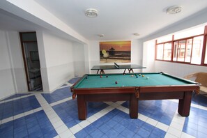 A pool table in a room with a blue and white tiled floor, a painting on the wall, and a window with blinds.