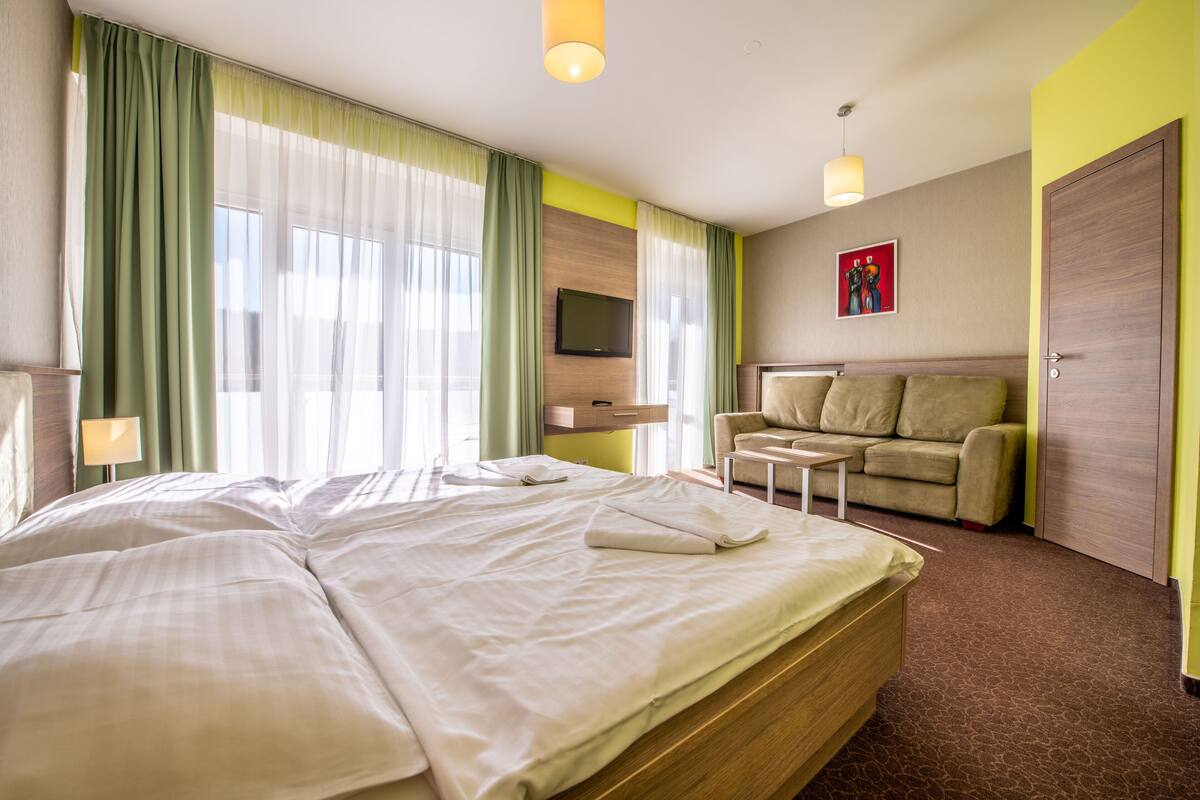 Quarto de hotel com uma cama grande, um sofá, uma televisão e um quadro na parede.